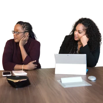 Two women in a meeting room listening to someone speak